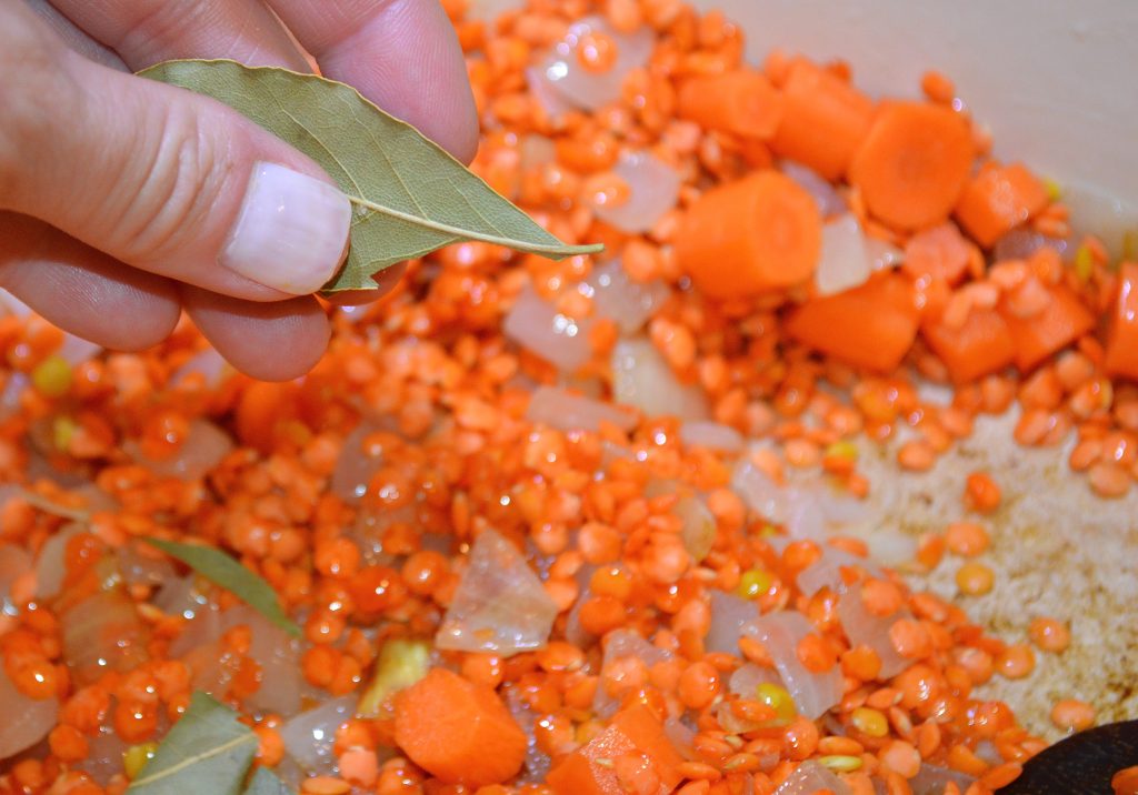 Adding bay leaf to lentils, carrots, onions and spices